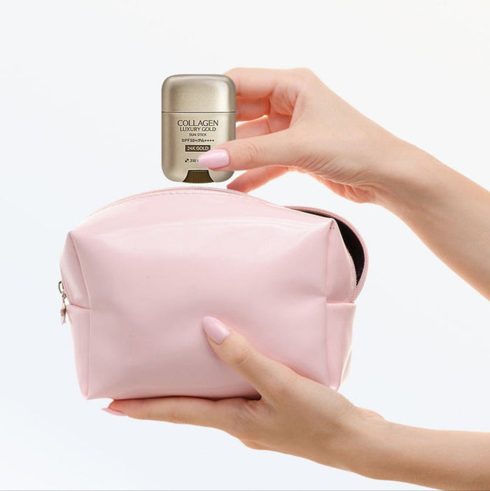 Hand holding 3W CLINIC Collagen & Luxury Gold Sun Stick 18g above a pink cosmetic bag