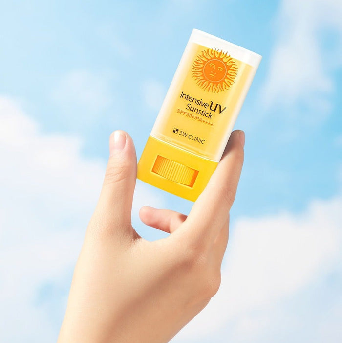 Hand holding 3W CLINIC Intensive UV Sun Sticks 20g against a blue sky background.