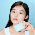 Woman holding ALTERNATIVE STEREO Soap Nude Cushion SPF42 PA++ against a blue background