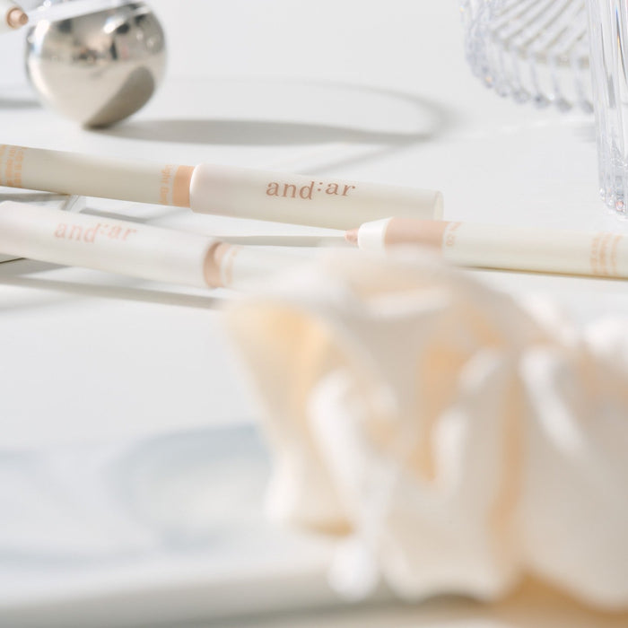 Close-up of the AND:AR Soft Skinfit Dual Concealer Pencil on a white surface, showcasing its sleek design and dual-end functionality.