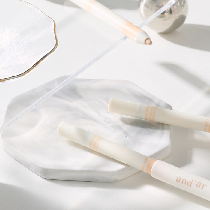 AND:AR Soft Skinfit Dual Concealer Pencil on a marble surface, showcasing sleek design and packaging.