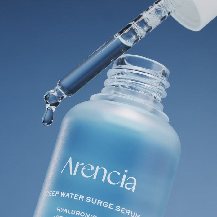 Close-up of ARENCIA Deep Water Surge Serum 30ml bottle with dropper releasing serum.