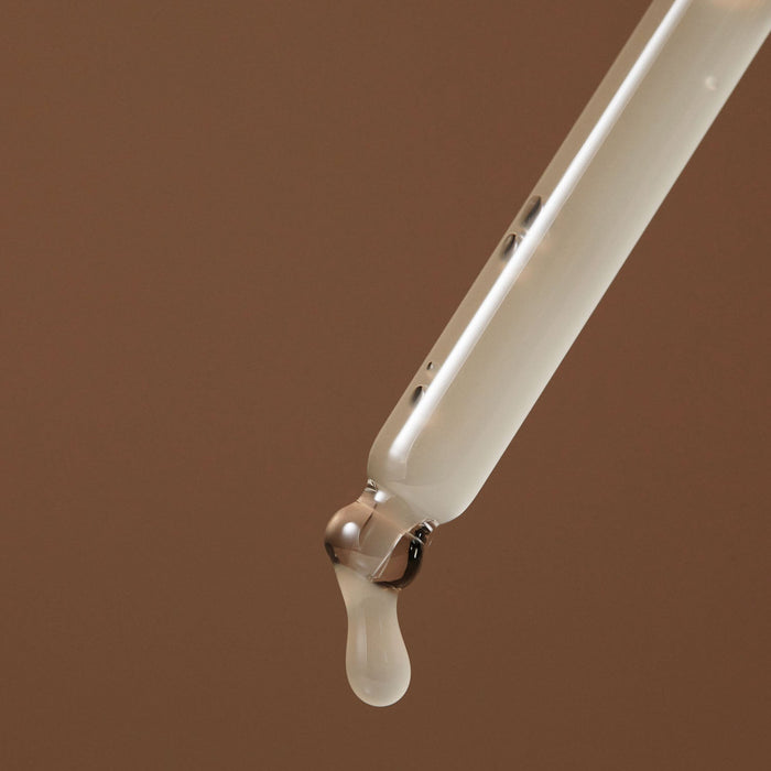 Droplet emerging from a pipette containing AROMATICA Vitalizing Rosemary Elasticity Ampoule 30ML on a brown background.