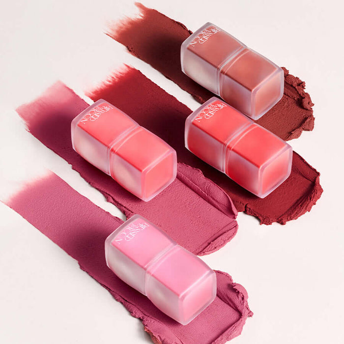 Assorted shades of BLESSED MOON Veil Blur Lip Tint on a textured surface.