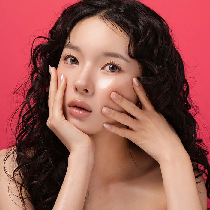 Model showcasing radiant skin using BLESSED MOON Veil Melting Glass Highlighter on a vibrant red background.