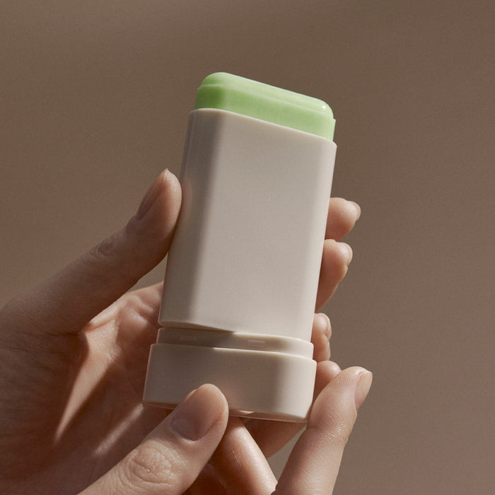 BLITHE Ice Sunscreen Stick held in hand, showing the product's design and green top in a neutral background setting.