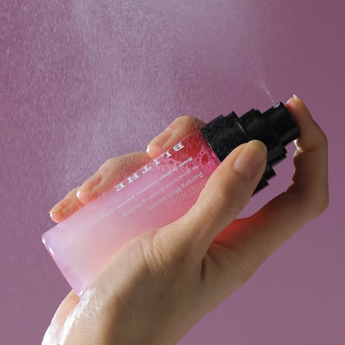 Hand holding BLITHE Inbetween Aurora Mist Serum 82ml against a pink background, showcasing its misting action.