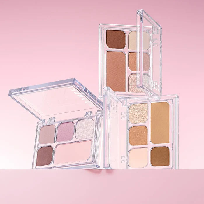 COSNORI My Moment Eye Palette featuring a range of neutral and shimmer eyeshadows in open compact cases on a pink background.
