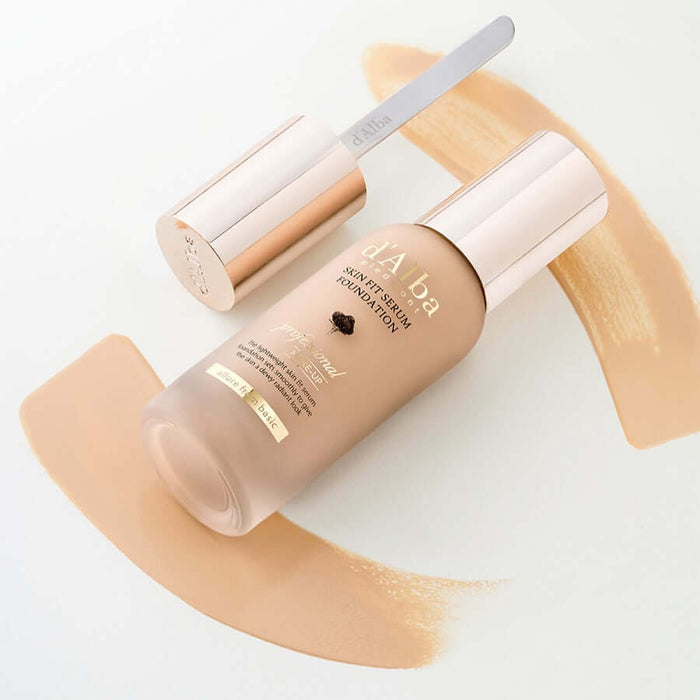 D'ALBA Vegan Skin Fit Serum Foundation bottle with applicator on a background of foundation swatches.