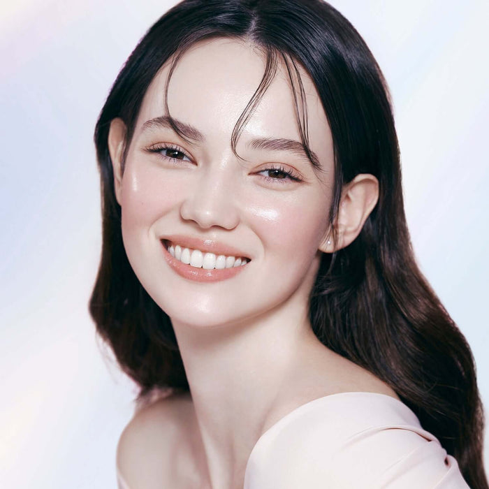 Woman with radiant skin wearing DEAR DAHLIA Prime Layer Glow Primer, showcasing makeup benefits.