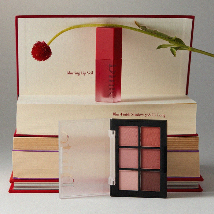 DINTO Blurring Lip Veil with palette on books, showcasing beauty products.