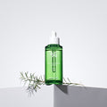 Green bottle of DR.CEURACLE Tea Tree Purifine Essence 50ml with white dropper on a white background with tea tree leaves.