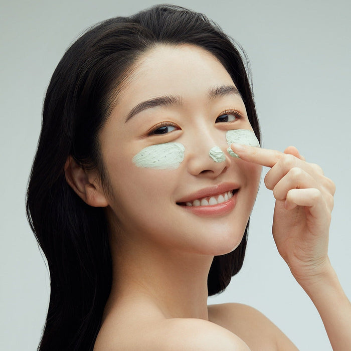 Woman applying FULLY Green Tomato Clay Pack Cleanser 120ml to her face, smiling, demonstrating skincare benefits.