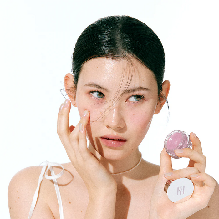 Woman applying HERA Sensual Lip & Cheek 7g to her cheeks, showcasing versatile makeup use.