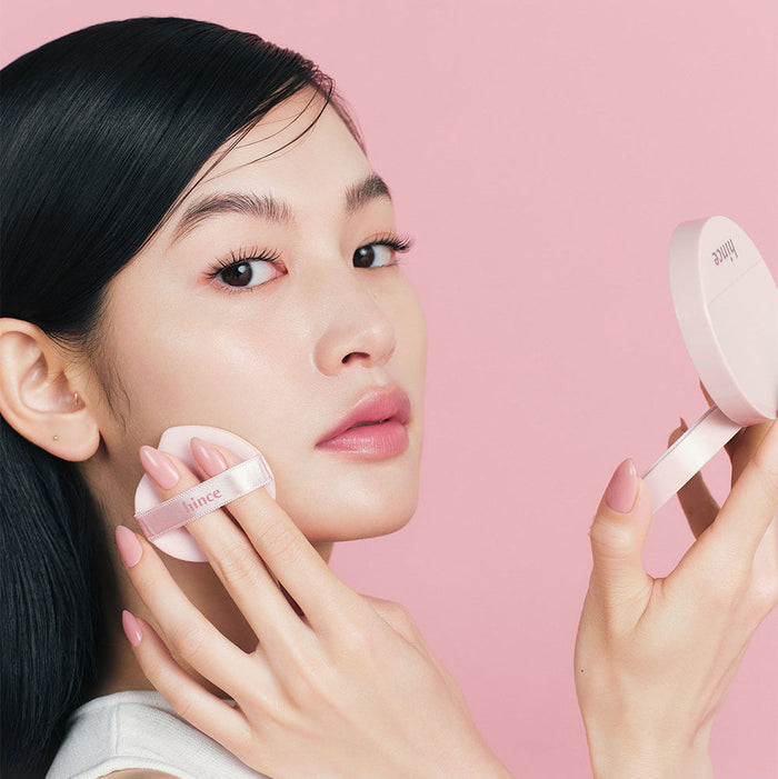 Model applying HINCE Cover Master Pink Cushion on face, showcasing radiant finish and smooth application for flawless skin.