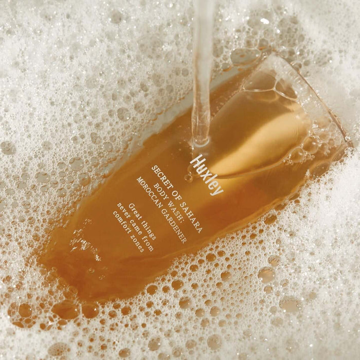 HUXLEY Body Wash Blue Medina Tangerine in foamy bath setting, showcasing luxurious bottle design and branding in use.