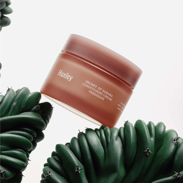 HUXLEY Conditioning Cream Preshape in a brown jar surrounded by green succulents