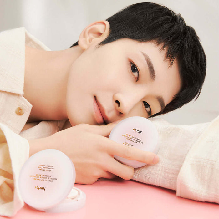 Person holding HUXLEY Essence Cover Cushion Unseen Layer compact with smooth skin and a gentle smile.