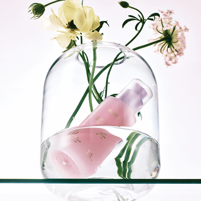 HUXLEY Skin Glow Essence Vita Radiance bottle with flowers under glass dome