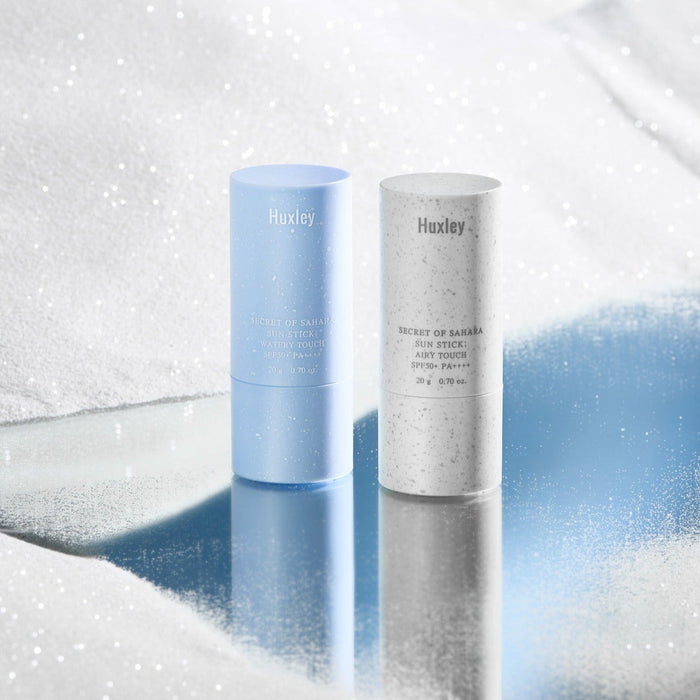 HUXLEY Sun Stick Watery Touch 20g on reflective surface with snow-like background.