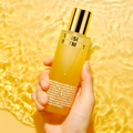 Hand holding ISOI Intensive Treatment Essence 130ml bottle against a golden background.