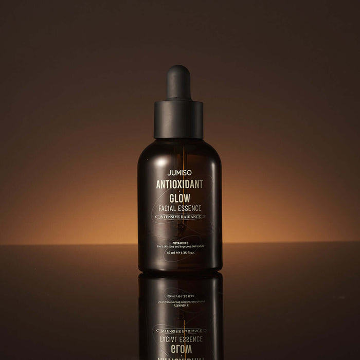 JUMISO Antioxidant Glow Facial Essence bottle on a reflective surface with a warm background