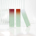 Three KAINE Glow Melting Lip Balm tubes standing on a reflective surface with a clear glass backdrop.