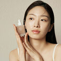 Woman holding KAINE Kombu Barrier Ampoule close to her face, showcasing skincare product and packaging.