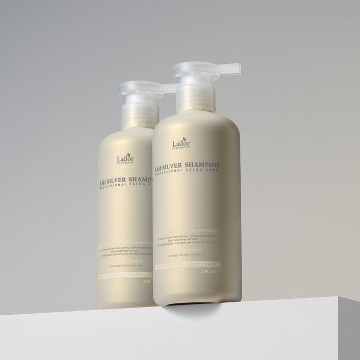 Two bottles of LADOR ASH Silver Shampoo 300ml displayed on a white surface with a neutral background.