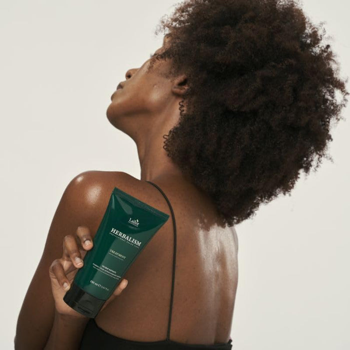 Woman holding LADOR Herbalism Treatment 150ml with visible product label