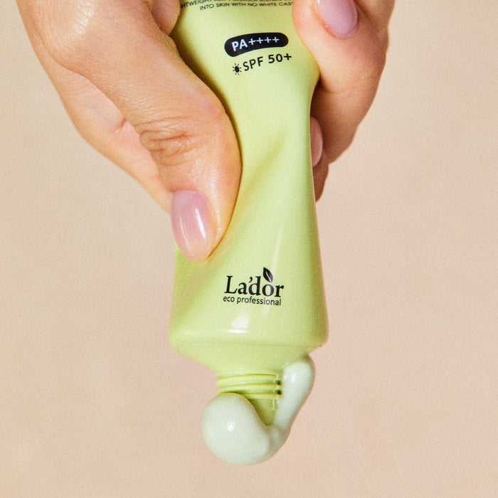 Hand squeezing LADOR Tamanu Airy Sunscreen 50ml with SPF 50+ onto palm, green tube, eco-friendly skincare product for sun protection.