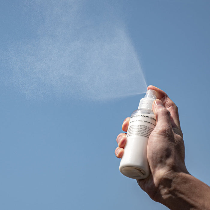 LAZY SOCIETY All-in-One Cream Spray 120ml being sprayed by a man’s hand against blue sky – Gentleman Korea Korean men’s skincare