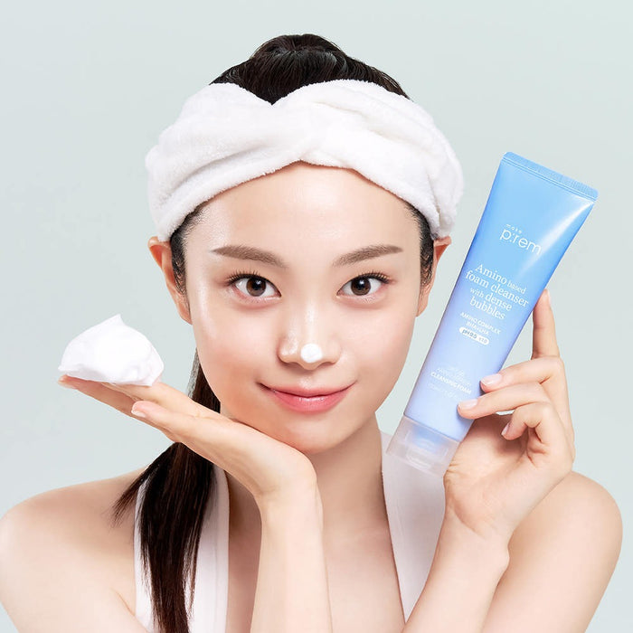 Person holding MAKE P:REM Safe Me Amino Refresh Cleansing Foam 150ml beside face, with cleansing foam on nose and headband on.