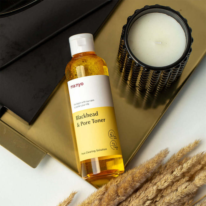 MANYO Blackhead & Pore Toner 210ml bottle on a gold tray next to a candle, featuring skincare benefits for blackheads and pores.