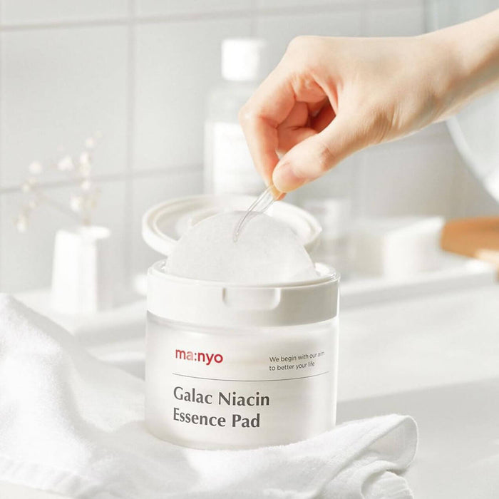 MANYO Galac Niacin Essence Pad 80 Sheets in a bathroom setting, showcasing a hand using the skincare product for facial care.