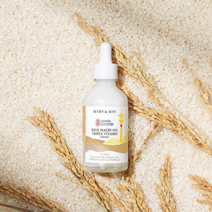 MARY & MAY Rice Niacin 10% triple Vitamin Serum bottle on rice background with wheat accents.