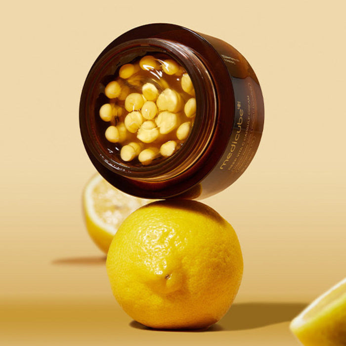 Open jar of MEDICUBE Deep Vita C Capsule Cream 55g with lemons in the background, showcasing skincare product ingredients.