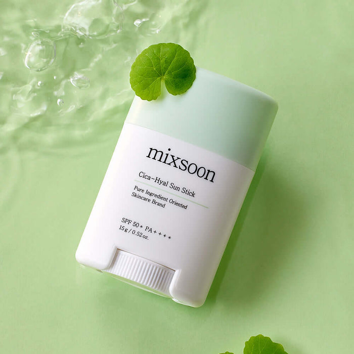 MIXSOON Cica Hyal Sun Stick with green cap, SPF 50+, on a light green background, surrounded by water droplets and a leaf.