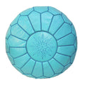 A round, turquoise Moroccan leather ottoman with intricate embroidered designs and a snowflake pattern in the center.