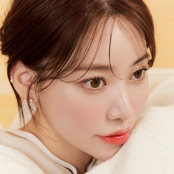 Close-up of a person with brown hair and warm skin tone, wearing a white sweater and pearl earrings, gazing thoughtfully.