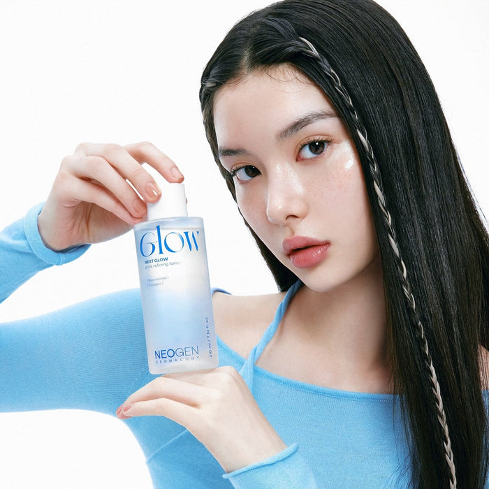 Person holding NEOGEN Next Glow Pore Refining Toner 210ml demonstrating skincare application in blue attire.