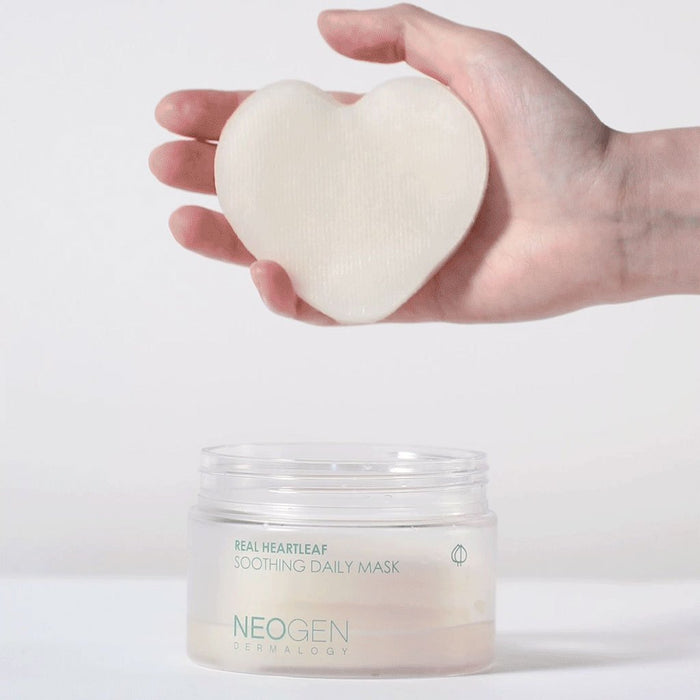 Hand holding NEOGEN Real Heartleaf Soothing Daily Mask 40 Sheets above open jar, showcasing heart-shaped pad for skincare.