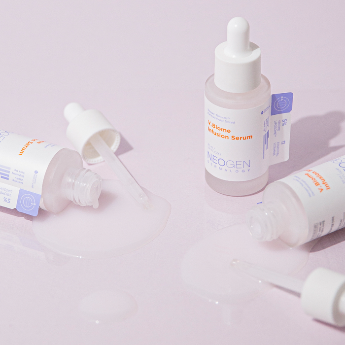 Bottles of NEOGEN V Biome Infusion Serum 30ml with droppers and serum spillage on a pastel surface.