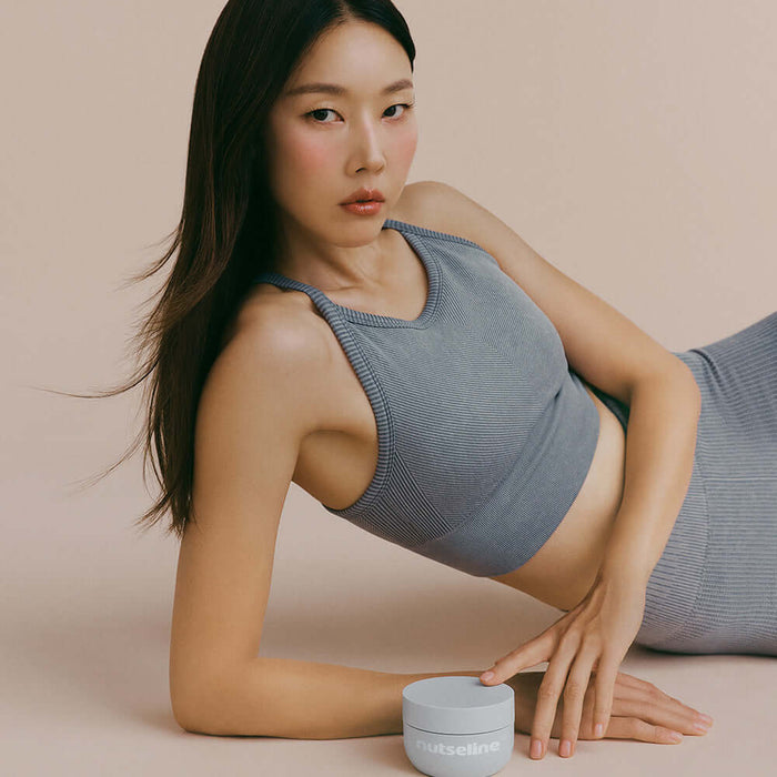 Woman posing with NUTSELINE Aroma Nut Gray Body Scrub 200g in a stylish setting.
