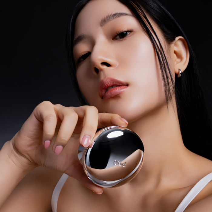 Woman holding OIAD Pore Perfecting Mirror Moon Cushion close to her face, showcasing skincare product's elegant design and functionality.