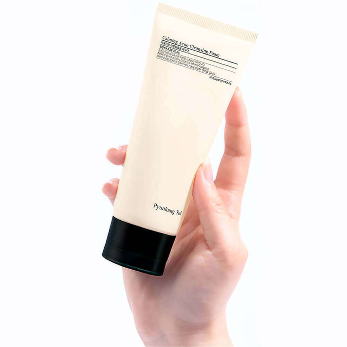 Hand holding PYUNKANG YUL Calming Acne Cleansing Foam 100ml tube on a white background.