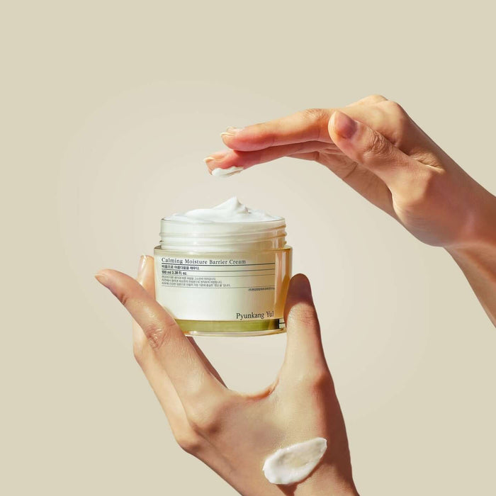 Hands holding and applying PYUNKANG YUL Calming Moisture Barrier Cream 100ml from a jar.