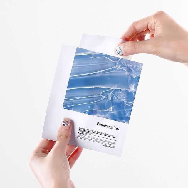 Person holding a PYUNKANG YUL High Moisture Essence Mask Pack demonstrating one of the 10 pieces included.