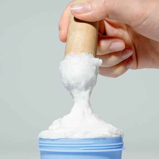 A hand holding a wooden spatula dipping into PYUNKANG YUL Pore Cleanser 100g, showing the creamy texture of the product.