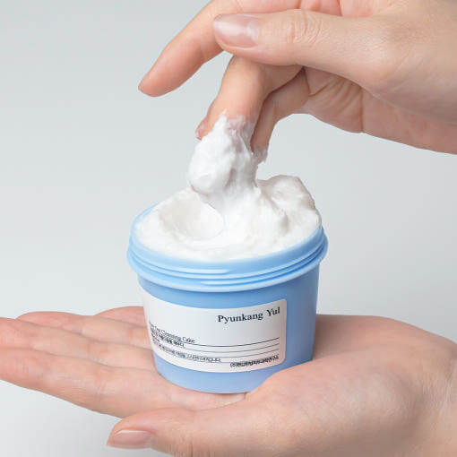 Hand holding PYUNKANG YUL Pore Cleanser 100g in blue jar with visible texture
